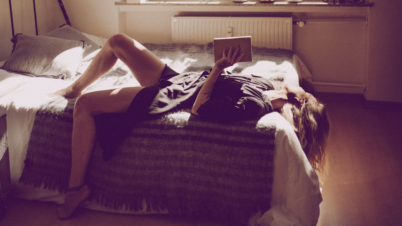 Frau, die im Sommer mit Buch auf ihrem Bett liegt