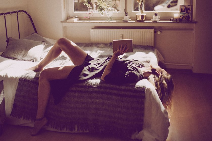 Frau, die im Sommer mit Buch auf ihrem Bett liegt