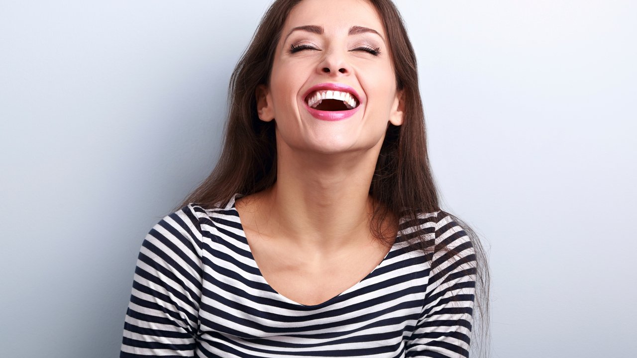 Happy natural laughing young casual woman with wide open mouth and closed eyes on blue background