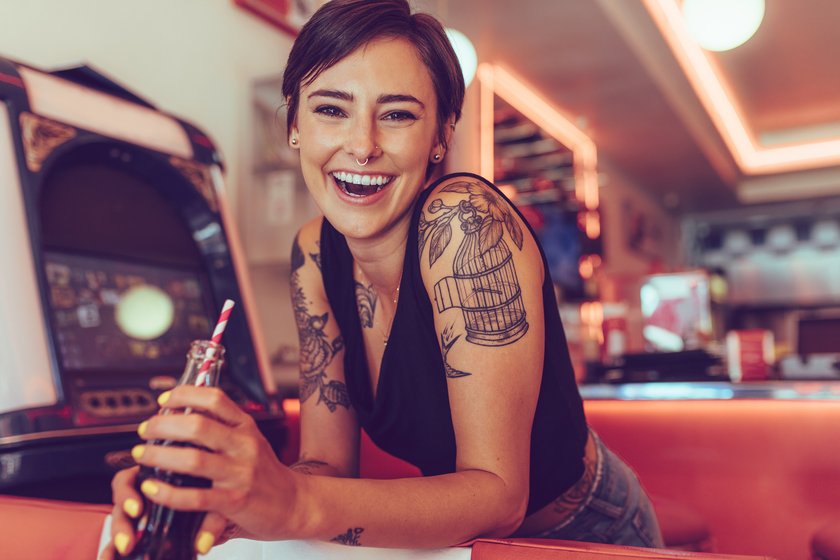 Frau mit Tattoos auf den Armen und einer Cola in der Hand
