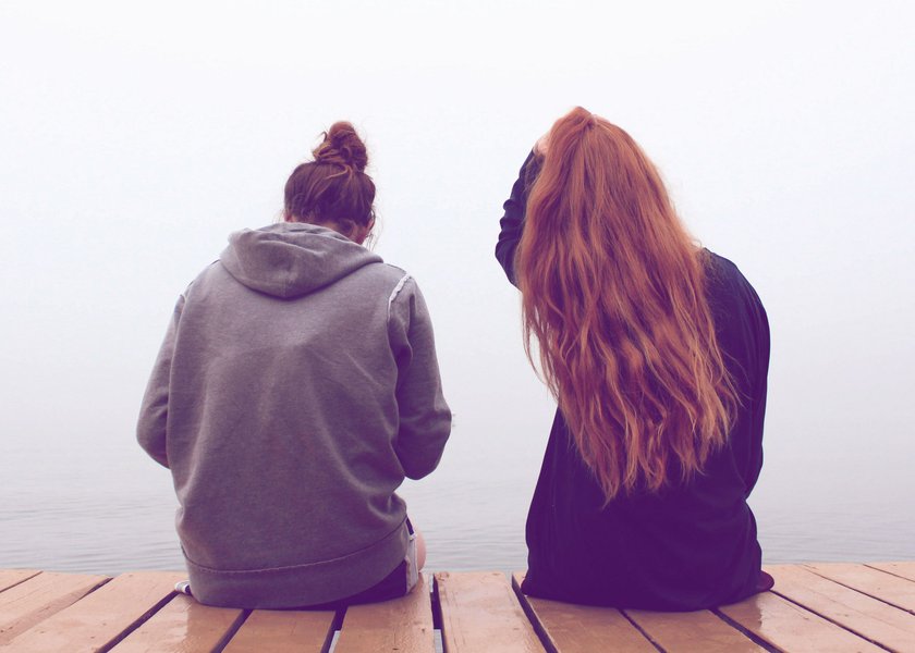 zwei Frauen, die an einem Steg sitzen und aufs Wasser schauen