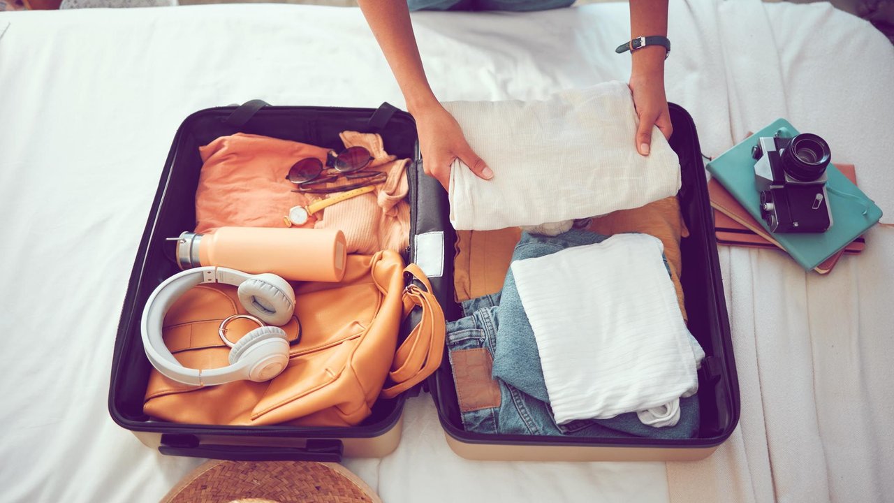 Travel packing, above and hands of a woman with clothes, holiday luggage and prepare for international summer. Suitcase, ready and person traveling with a suitcase, vacation clothing and hotel bag