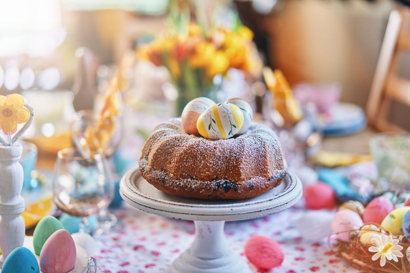 Ein gedeckter Tisch zu Ostern mit viel Deko und einem Osterkuchen auf einer Kuchenplatte