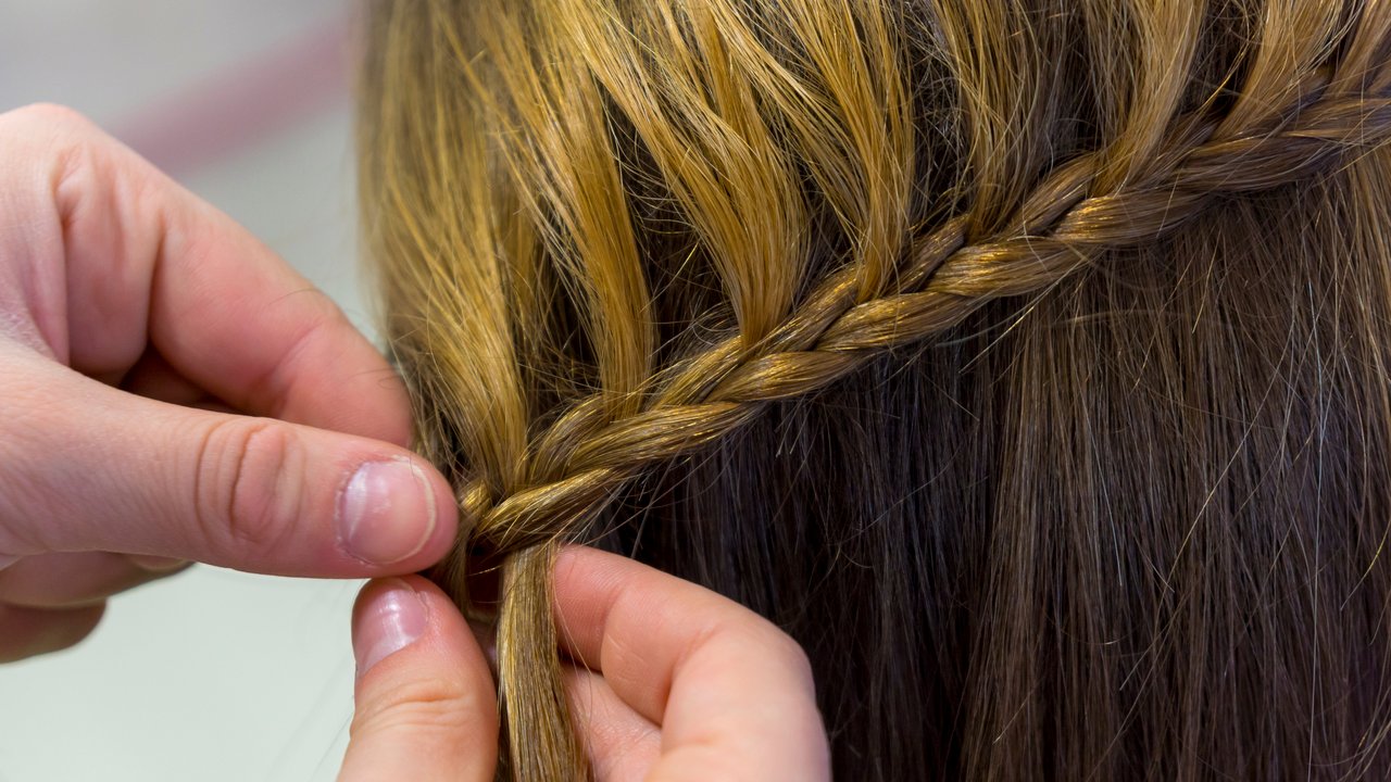 Hairdresser makes braids in beauty salon.