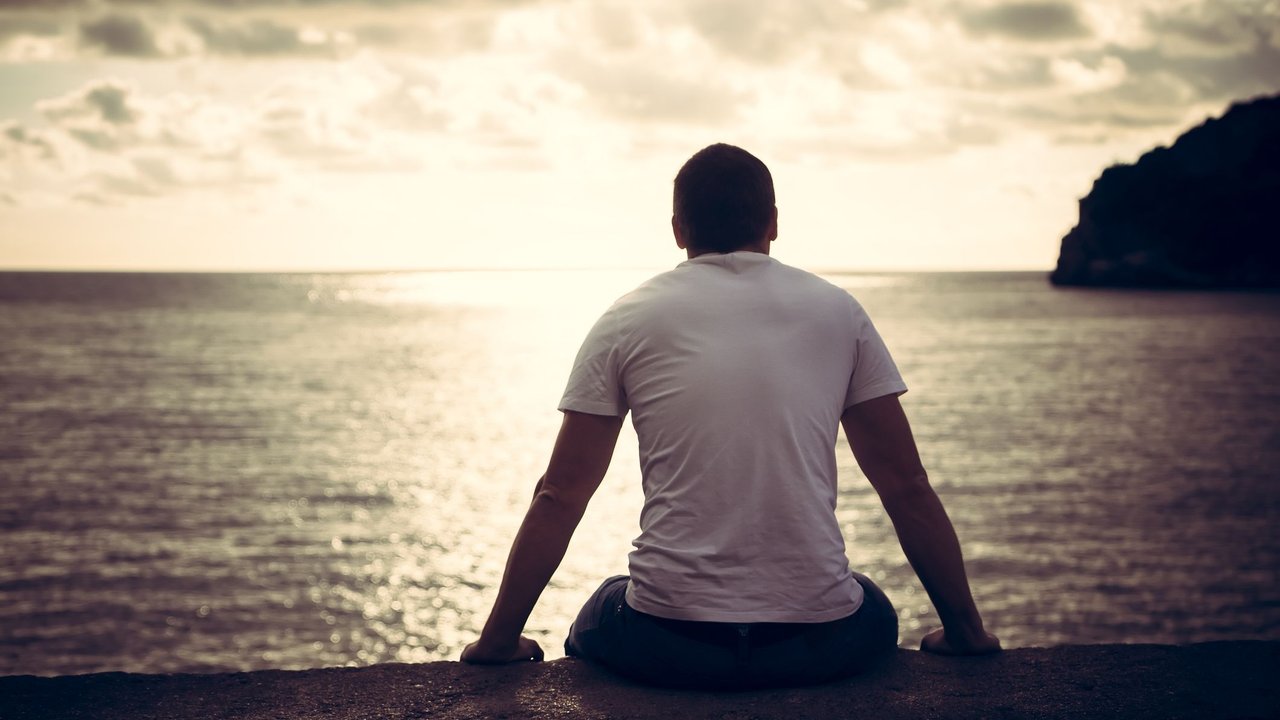 Rear view of lonely man looking with hope at horizon with sunlight during sunset with effect of light at the end of tunnel