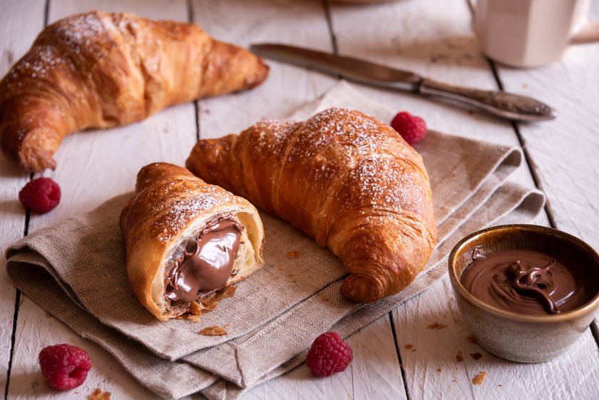 Baked sweet croissant with chocolate on white wooden table