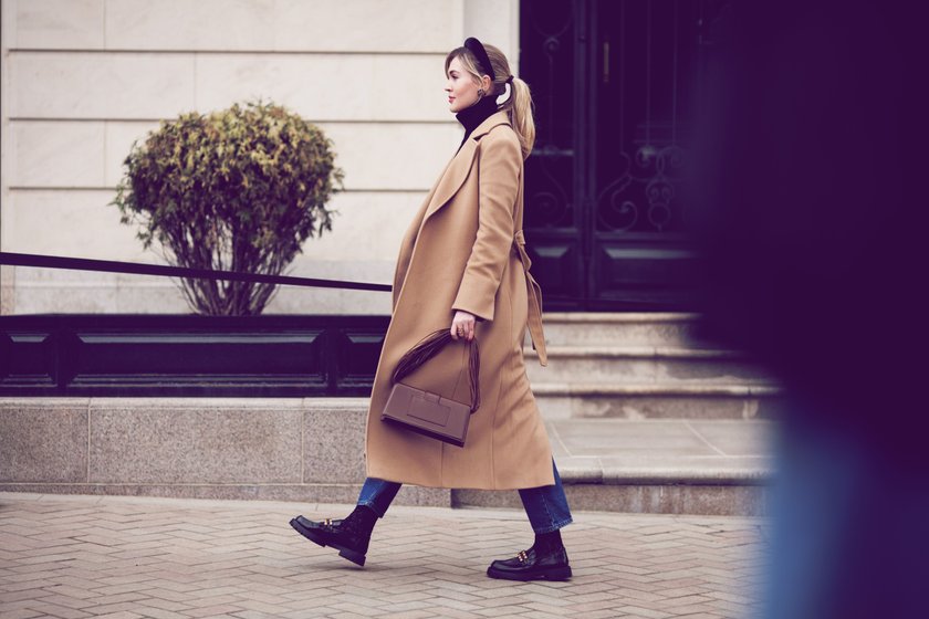 Side view beautiful woman walking street in fashionable spring or autumn clothes cashmere coat, jeans, loafers shoes and small bag. Full length Female model in motion, street style fashion