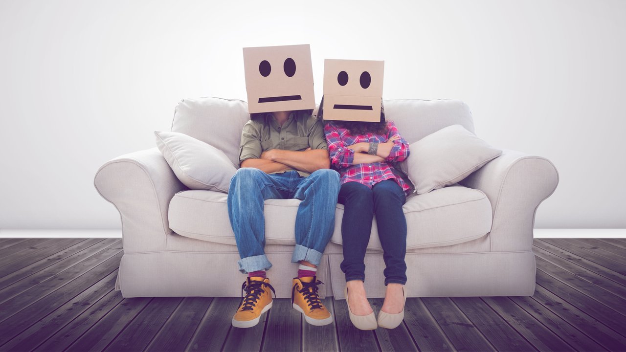 Couple sitting on couch with cardboard boxes over their head with smiley faces