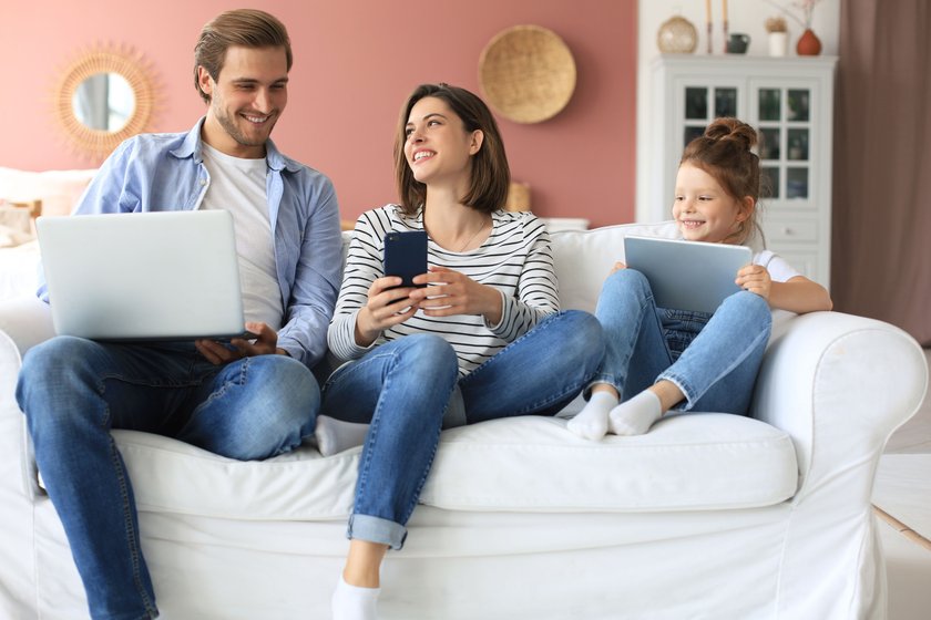 Familie auf der Couch an digitalen Geräten