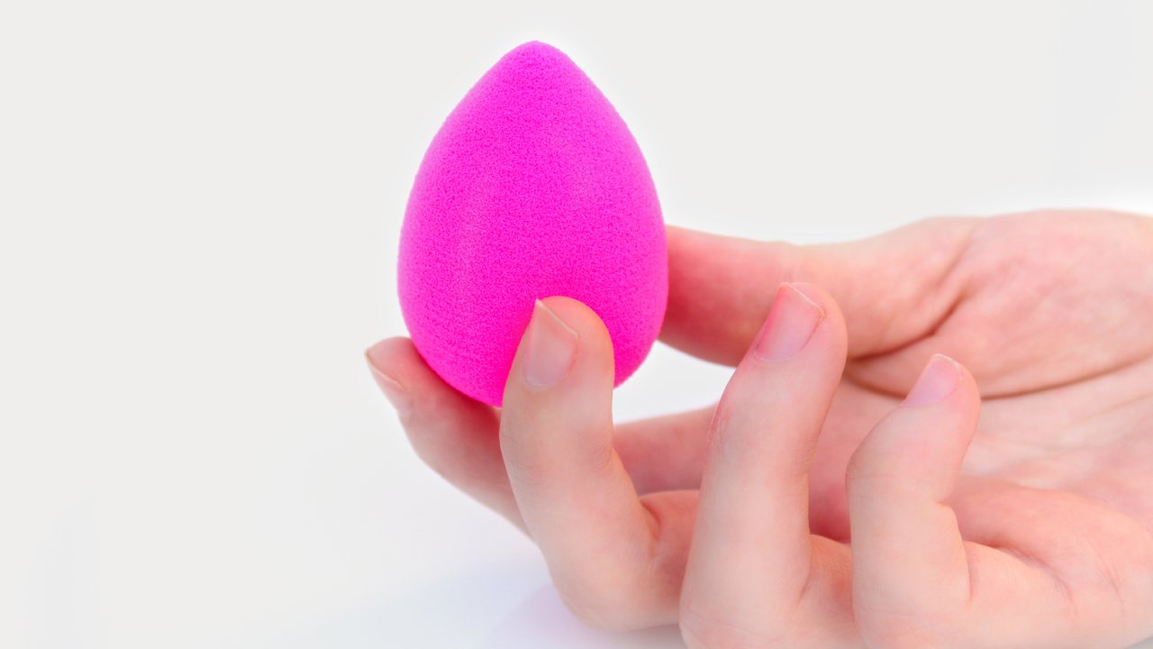 Hand holding a Pink makeup sponge isolated on white background