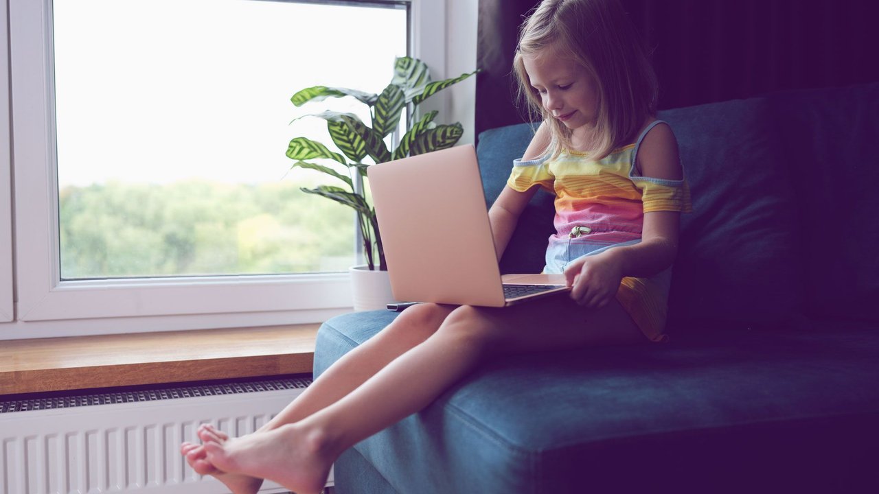 Kleines Mädchen sitzt mit Laptop auf Sessel