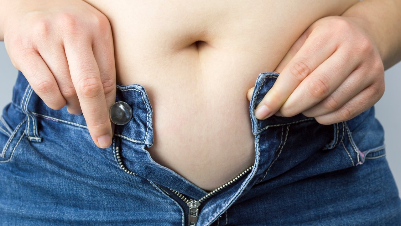 Cropped mid section of an obese woman trying to close the buttons of her jeans against a white background