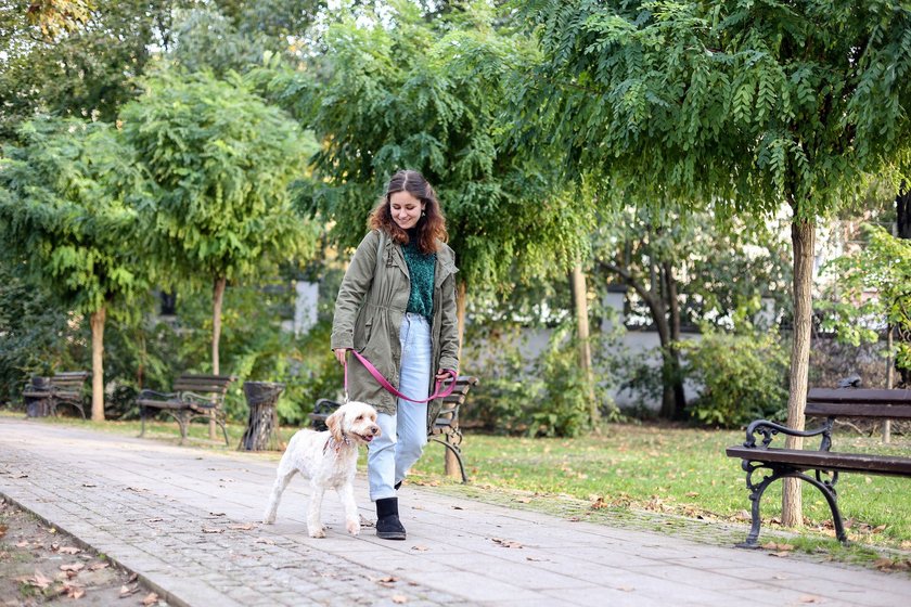 Young woman walking with her soft coated wheaten terrier dog in a park. About 25 years old, Caucasian female.