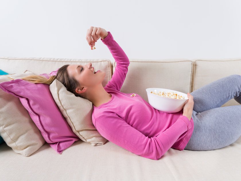 Frau liegt auf der Couch und isst Popcorn