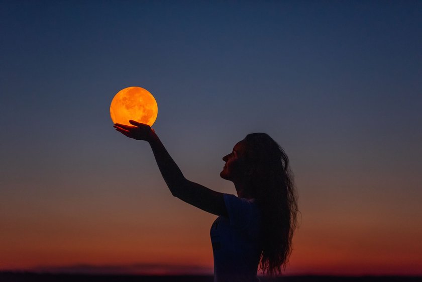 Junge Frau hält einen glühenden Mond am Himmel in den Händen