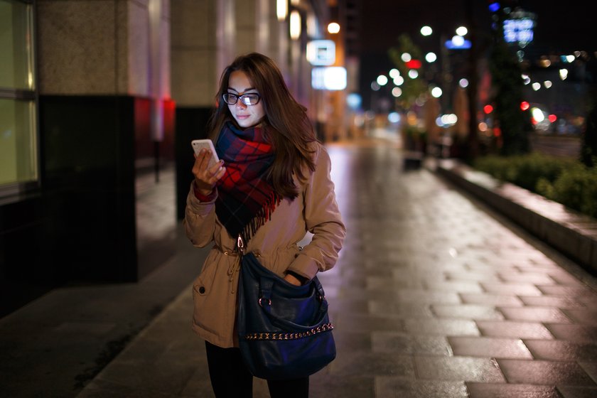 Frau läuft mit Handy nachts durch die Stadt