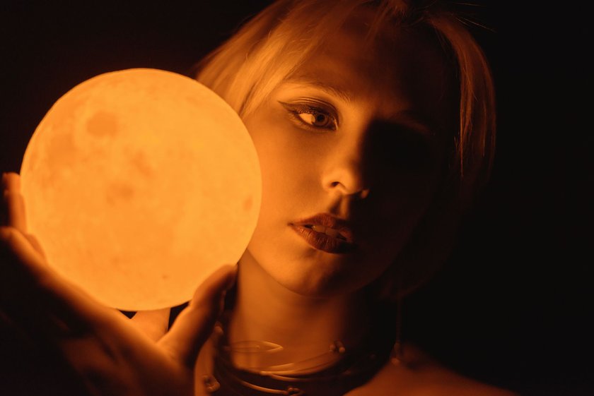 Woman holding a glowing sphere moon. Toned in warm color.