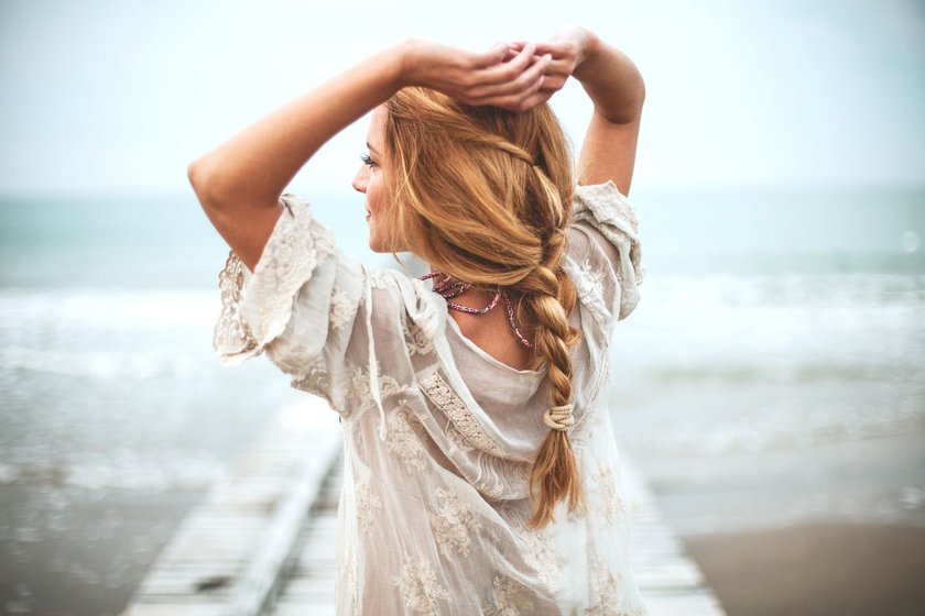 Eine Frau mit blonden Haaren und luftiger heller Kleidung am Strand