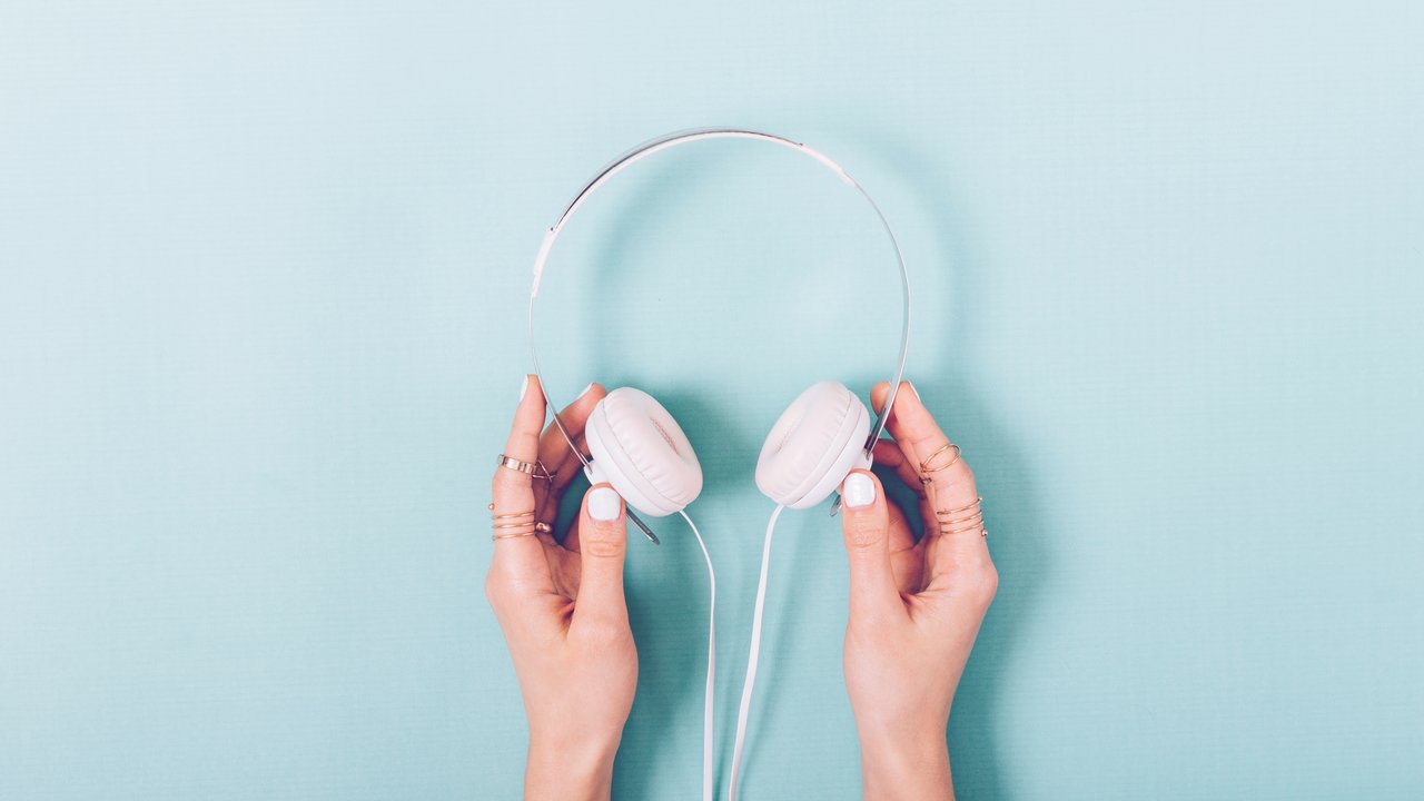White headphones in female hands with a manicure on a blue background top view