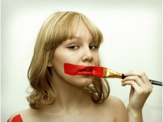 Frau, die sich mit einem breiten Pinsel einen dicken roten Streifen über den Mund malt Frau, die sich mit einem breiten Pinsel einen dicken roten Streifen über den Mund malt