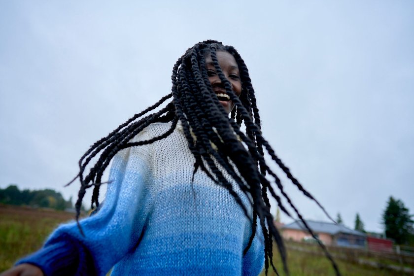 Eine junge Frau in einem blauen Pullover ist draußen und lächelt glücklich