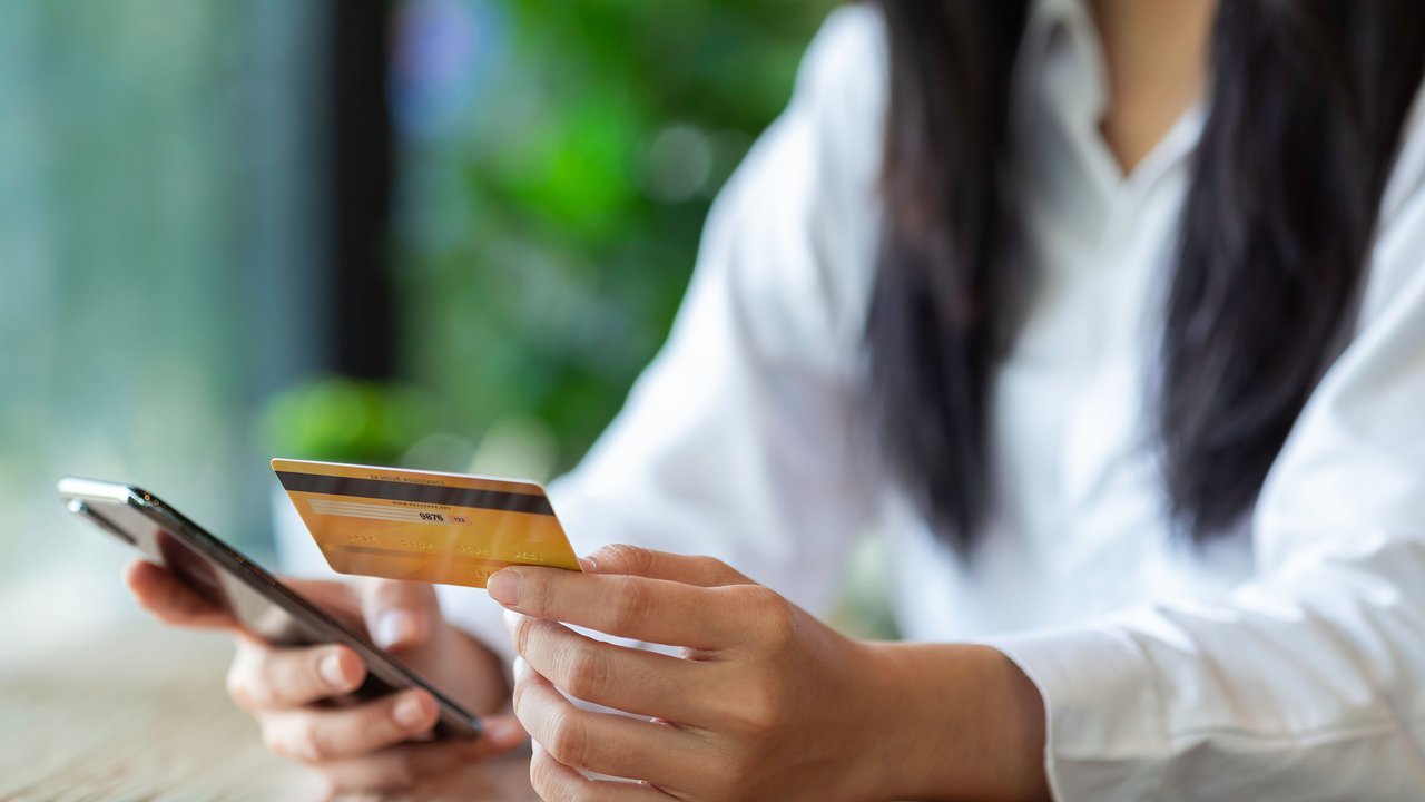 Hands of young Asian woman holding credit card and mobile phone for electronic payment in internet online remote store.