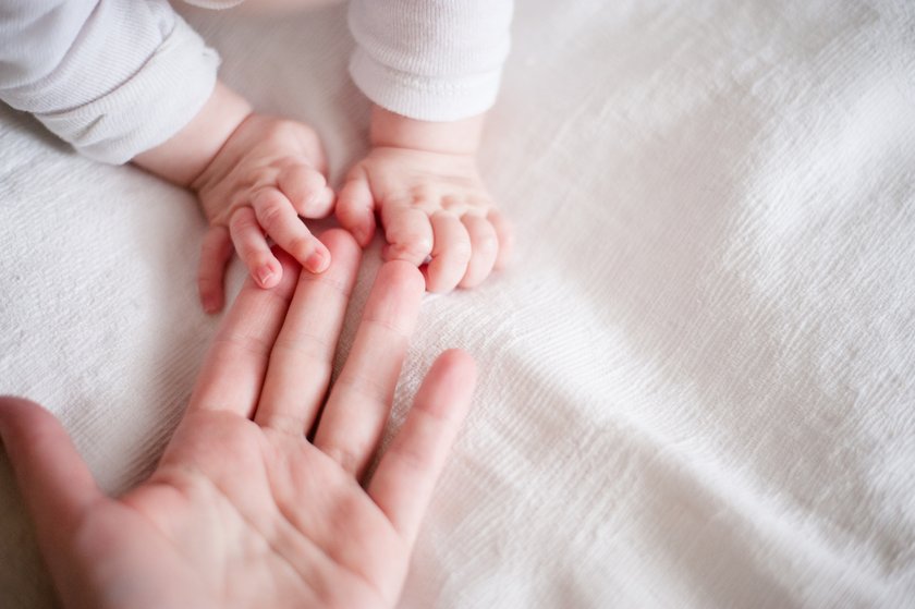 Die Hand eines Vaters berührt kleine Babyhände, die auf ihn zukrabbeln