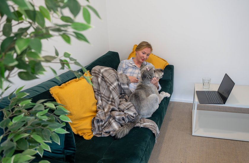 Frau liegt mit ihrem Hund auf dem Sofa.