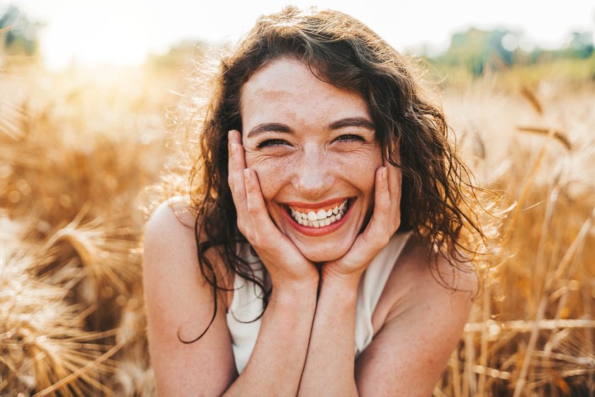 Eine Frau steht im Sommer im Feld und lächelt glücklich