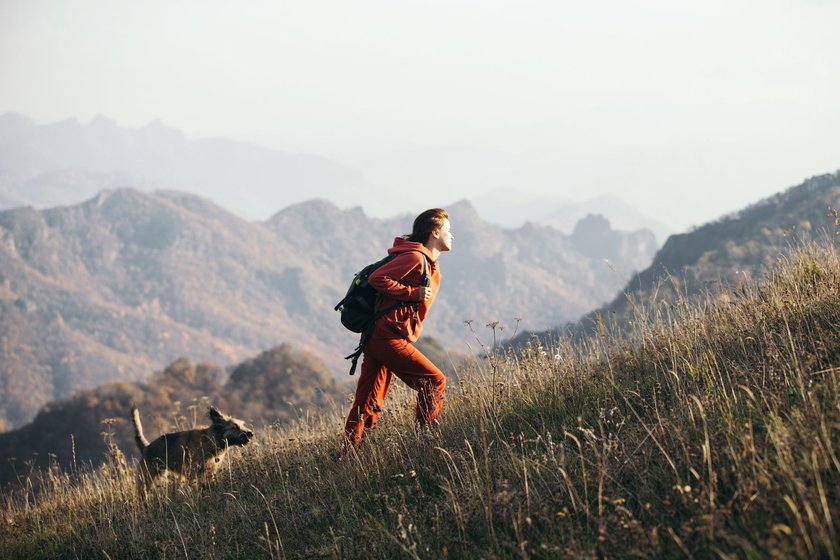 Eine Frau und ihr Hund wandern einen bergige Graslandschaft hinauf