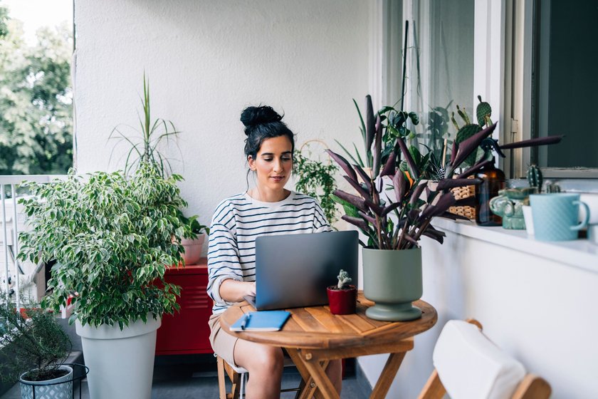 Young Caucasian woman sitting on her balcony, working on her laptop.
