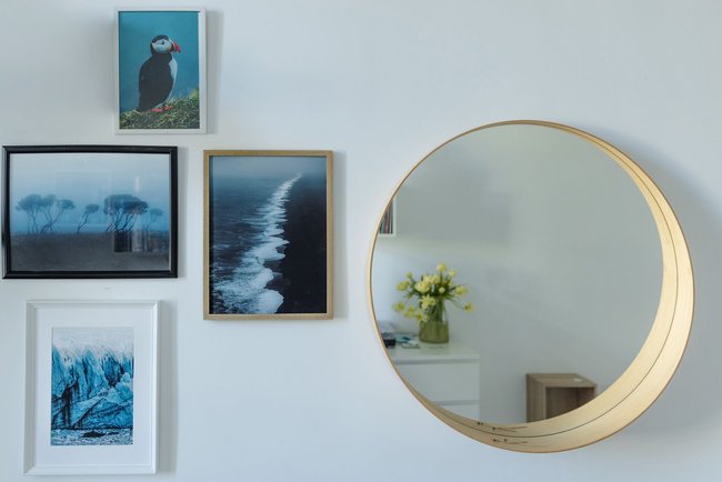 Part of Scandinavian style bedroom - Nordic photo prints in white, black and wooden frames and wooden round-shaped mirror on the wall