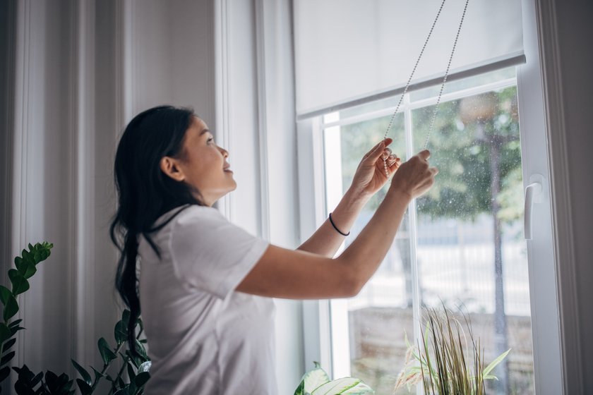 One&#x20;woman,&#x20;Asian&#x20;female&#x20;lowering&#x20;interior&#x20;blinds&#x20;on&#x20;window&#x20;at&#x20;home.