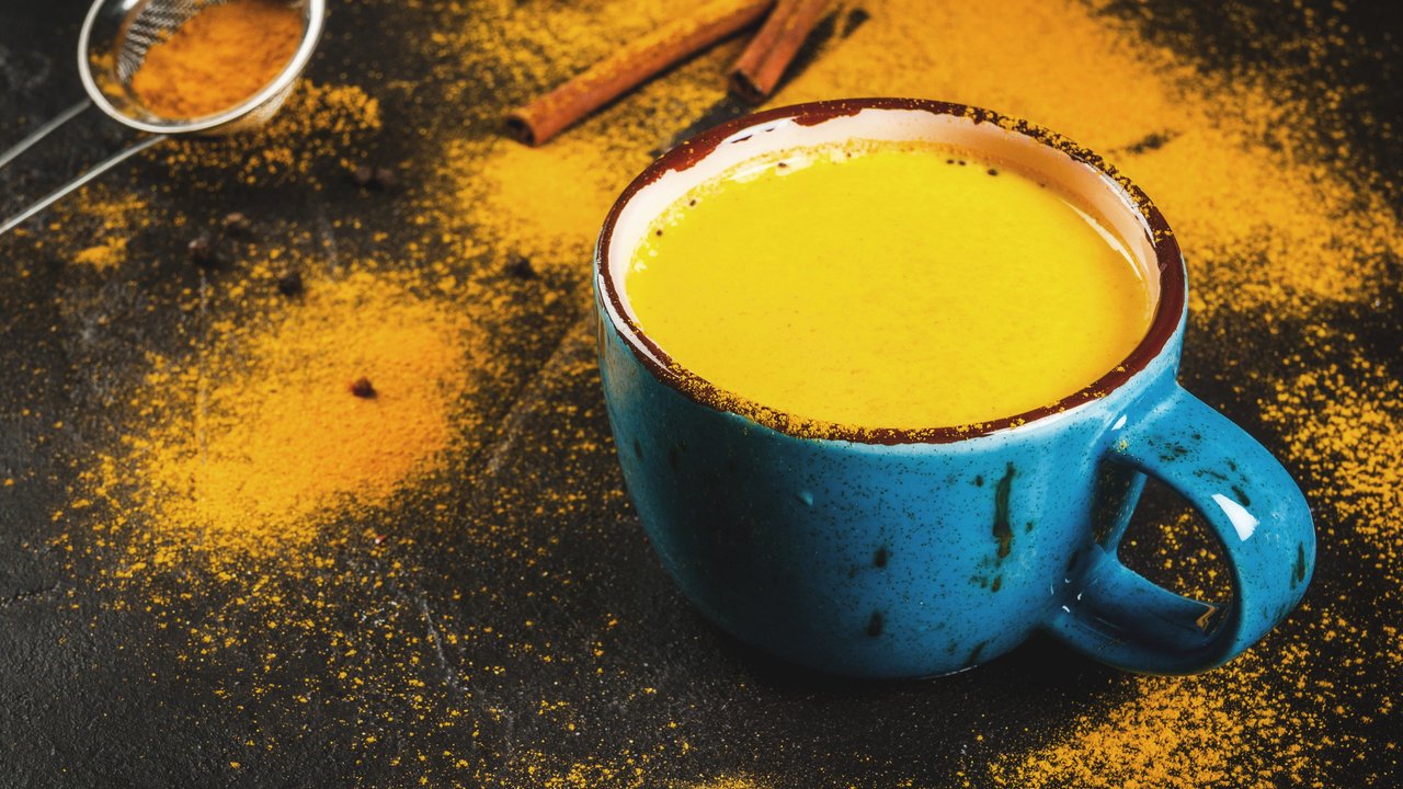 Traditional Indian drink turmeric milk is golden milk with cinnamon, cloves, pepper and turmeric. On a concrete table, with spices on the background. In a large cup, Copy space, toned