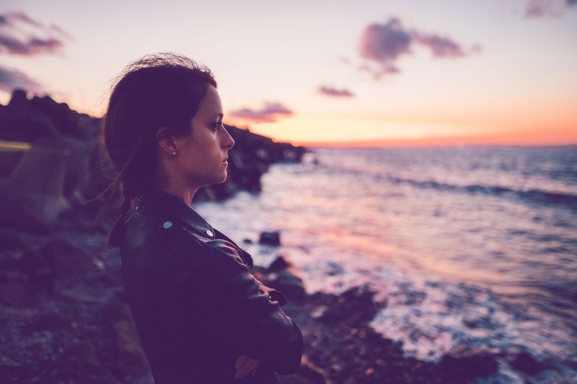 Frau steht bei Sonnenuntergang am Meer