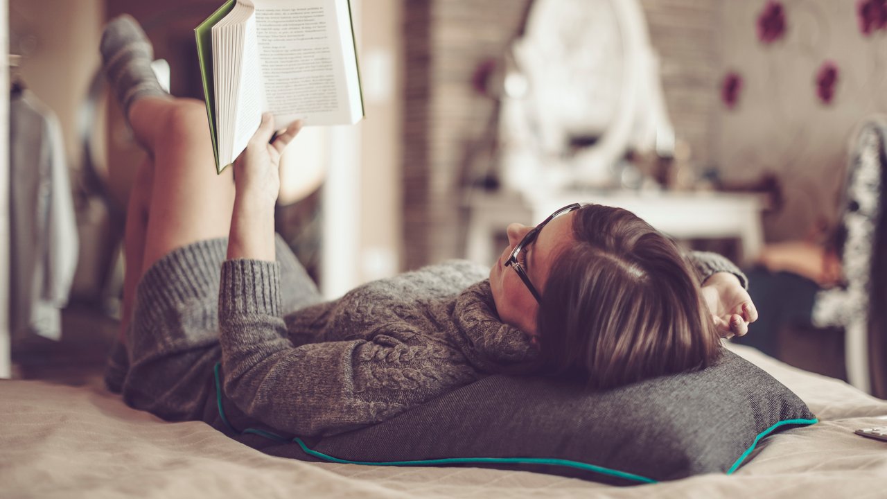 Schöne junge Frau liest zuhause auf dem Bett