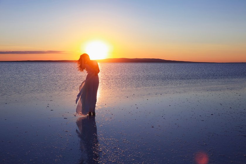 Eine Frau steht am einem See während die Sonne untergeht