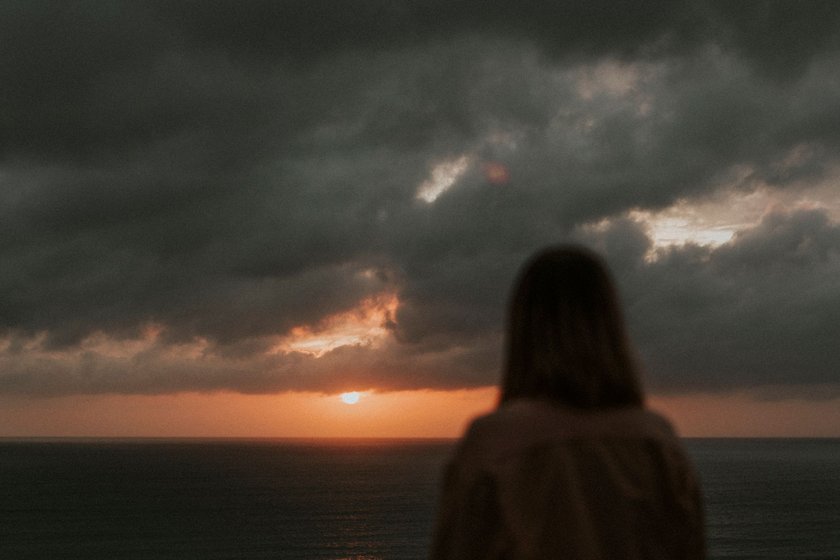 Eine Frau steht am Strand, während die Sonne an einem bewölktem Himmel aufgeht