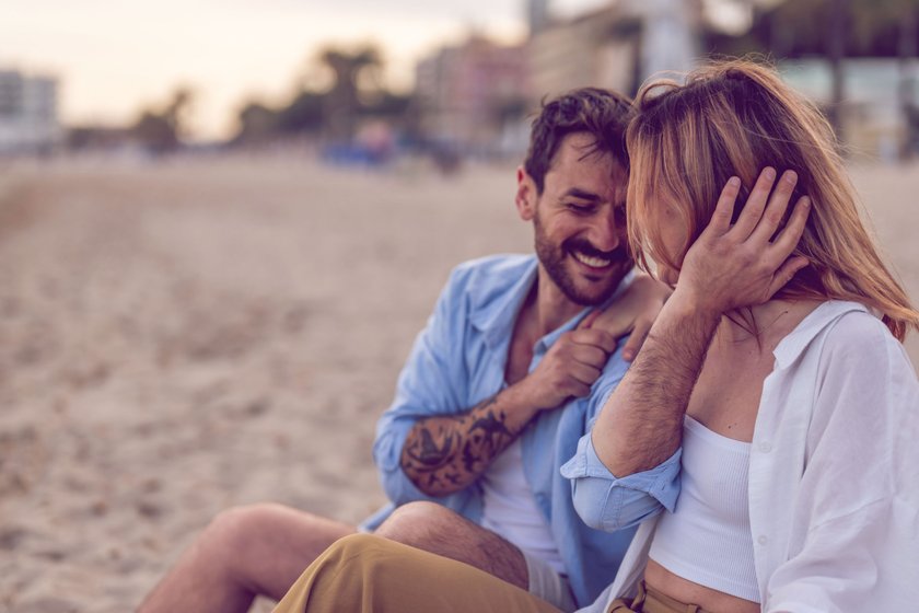 Paar sitzt am Strand und lacht zusammen