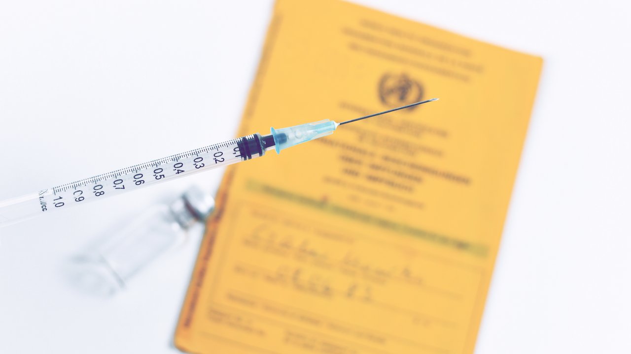 Vaccine concept with cclose up of empty syringe in front of blurry vial and yellow international certificate of vaccination in white background