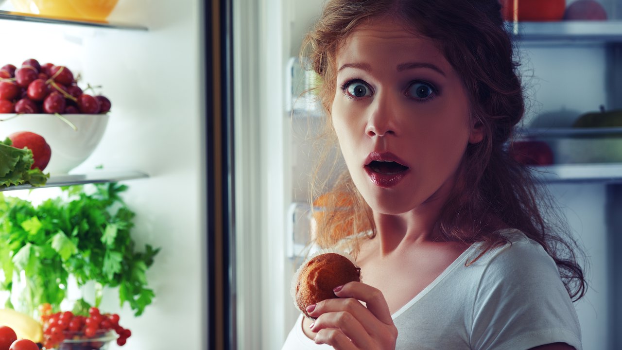woman eats sweets at night to sneak in a refrigerator