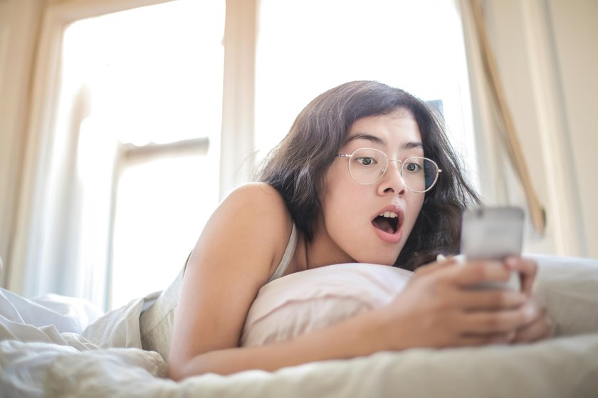 Frau liegend auf dem Bett mit Handy in der Hand 