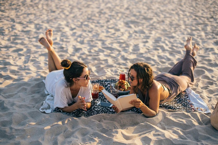 zwei Frauen, die auf Decke am Strand liegen und reden