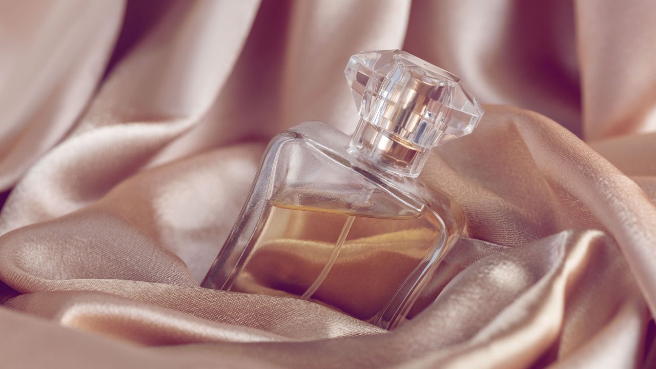 Ein Parfum-Flakon mit goldener Flüssigkeit umhüllt von einem seigen Tuch in einem Roséton