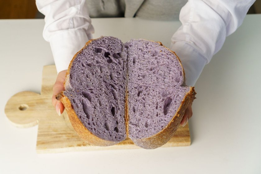 Purple Unusual and creative colored artisan sourdough bread in a cross section in the hands of a girl.