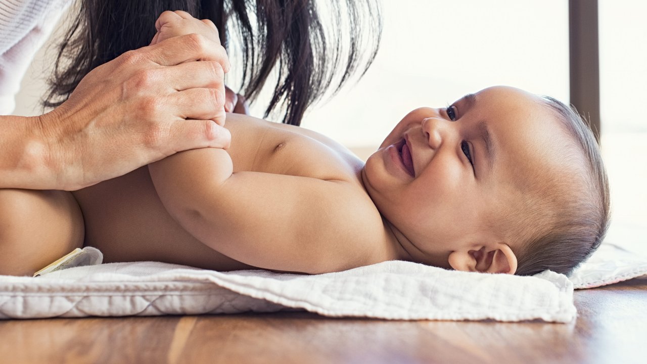 Happy mother playing with baby while changing his diaper. Smiling young woman with baby son on changing table at home. Close up of cheerful mom and toddler boy playing together.
