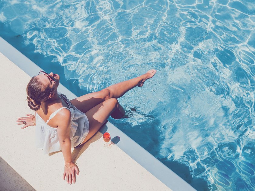 Frau sitzt mit Cocktail am Pool