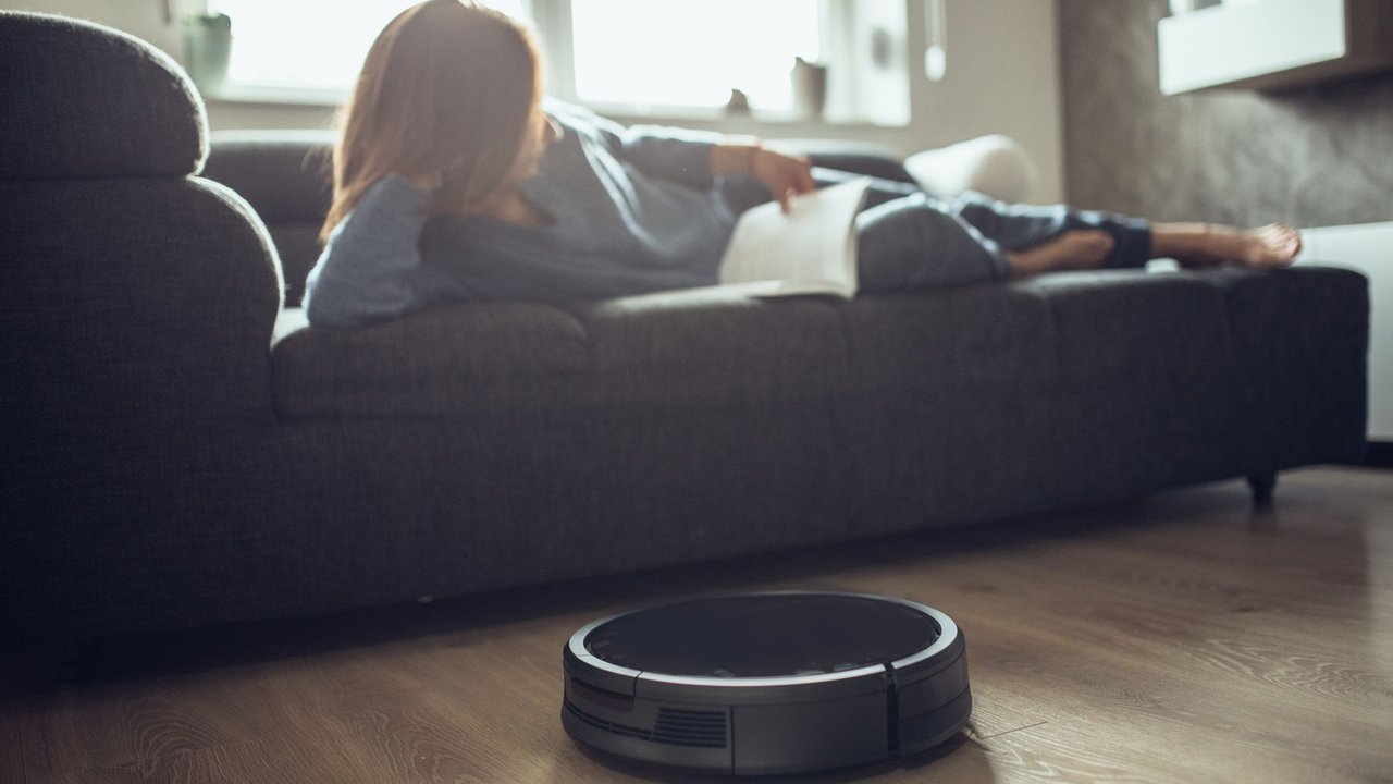 Robotic Vacuum Cleaner Cleaning Floor While Woman reading book