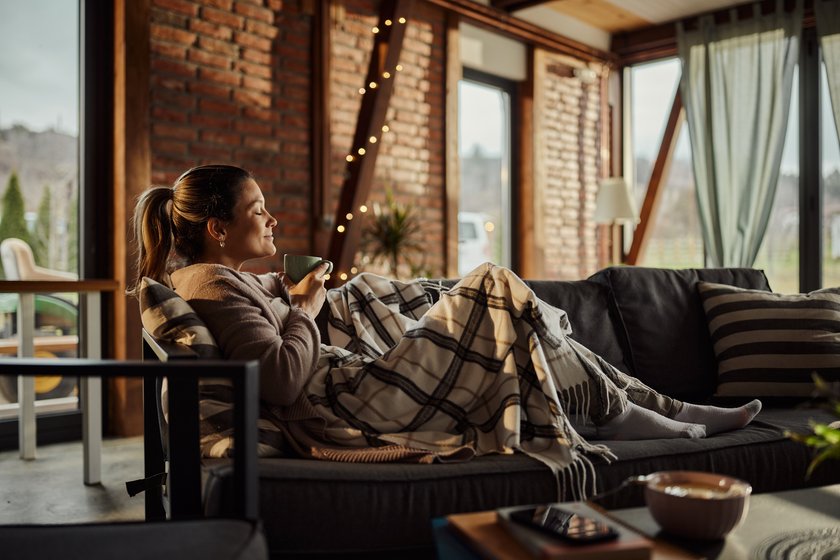 Smiling woman enjoying in the smell of fresh coffee while relaxing on sofa at home.