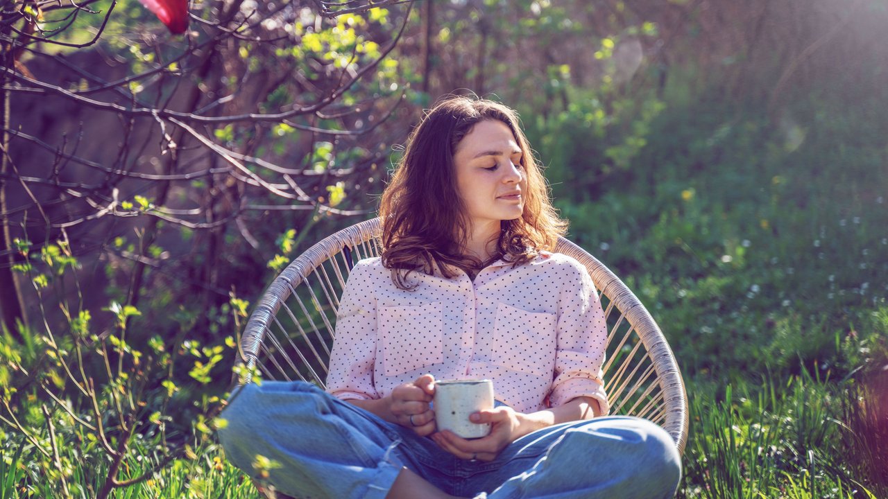 Frau sitzt im Garten mit Tasse in der Hand